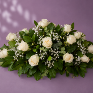 Cojín fúnebre con rosas blancas, follaje verde y flores de relleno en un arreglo floral elegante.