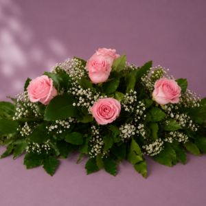 Cojín fúnebre con rosas rosadas, follaje verde y flores de relleno en un elegante arreglo floral.
