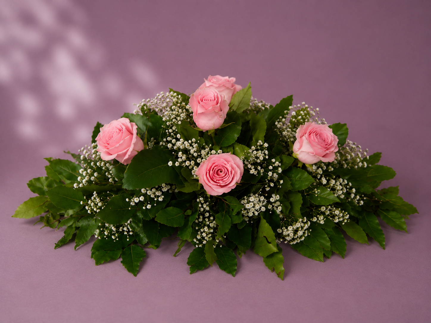 Cojín fúnebre con rosas rosadas, follaje verde y flores de relleno en un elegante arreglo floral.