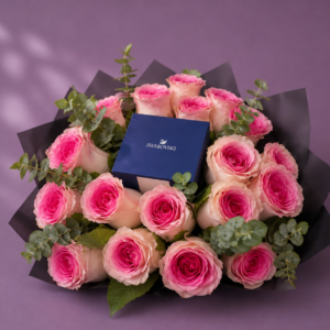 Arreglo floral con rosas rosadas, follaje verde y caja de joyería azul en el centro.