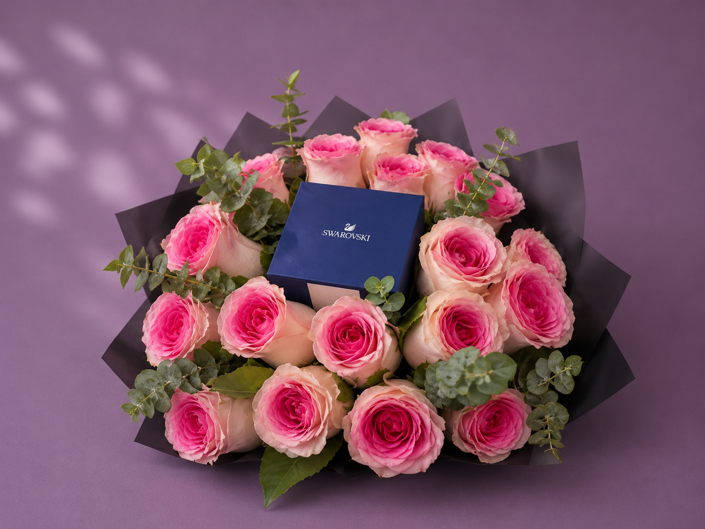 Arreglo floral con rosas rosadas, follaje verde y caja de joyería azul en el centro.