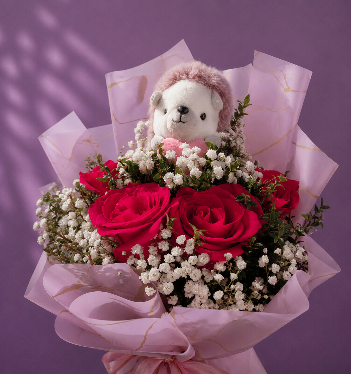 Ramo de rosas rojas con gipsofila, follaje verde y peluche decorativo en envoltorio rosado.
