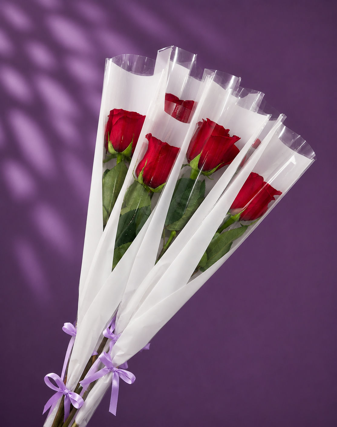 Rosas individuales rojas con envoltorio blanco, acabado transparente y lazo lila.
