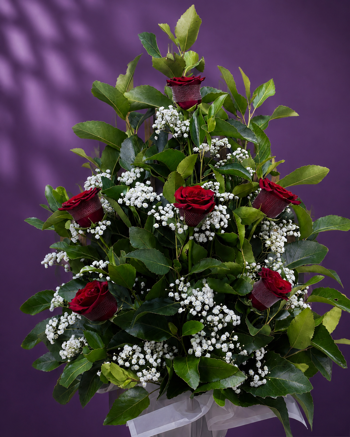 Pie de urna con 6 rosas rojas, follaje verde y gipsofila en un elegante arreglo floral.