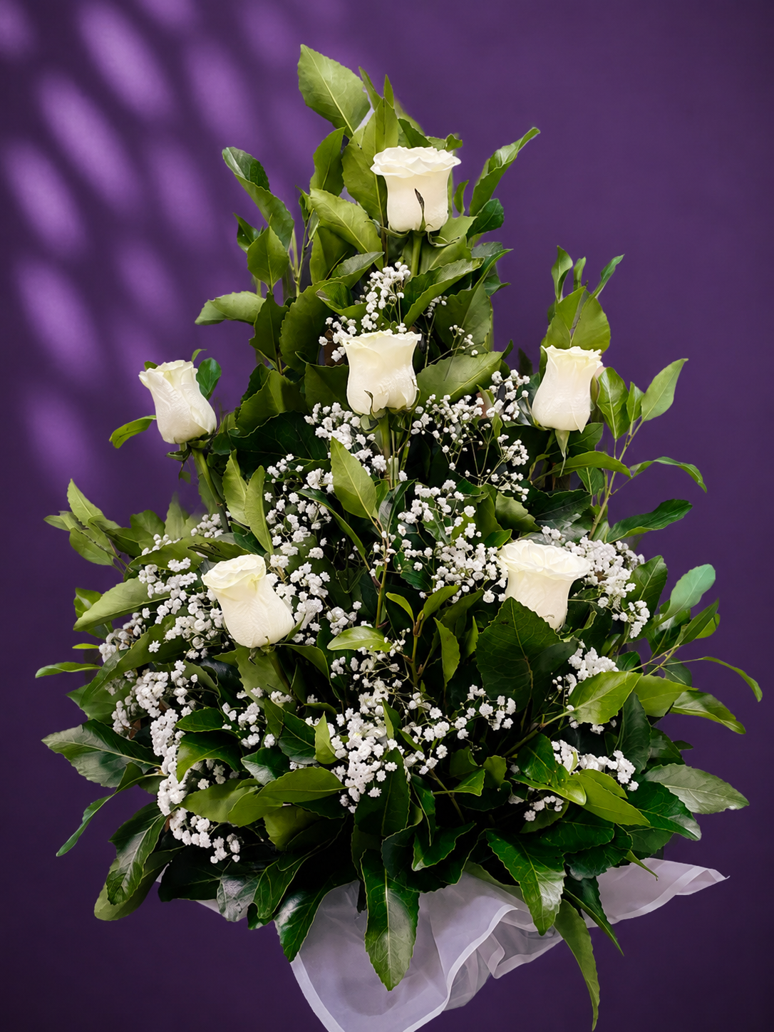 Pie de urna con 9 rosas blancas, follaje verde y gipsofila en un elegante arreglo floral.
