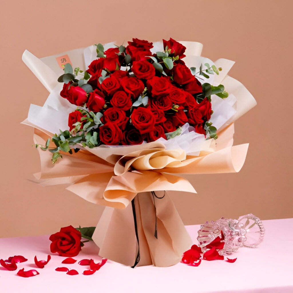 Ramo de rosas rojas con follaje verde y envoltorio elegante en tonos beige y blanco.