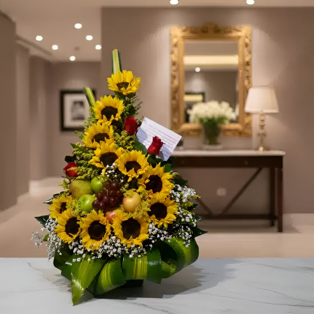 Arreglo floral con girasoles, frutas frescas y detalles decorativos en una elegante presentación.